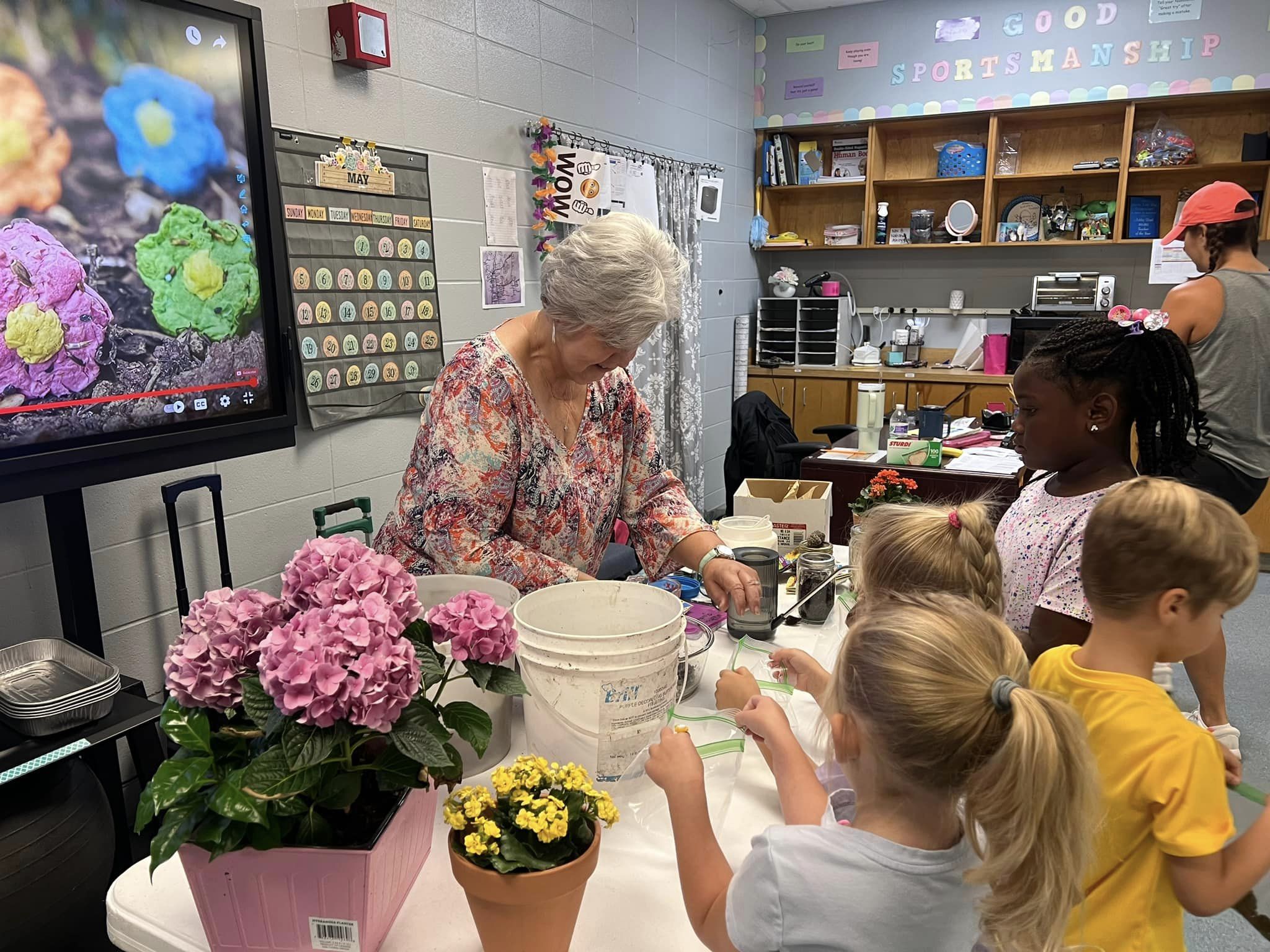 Students and teacher at a table with flowers.